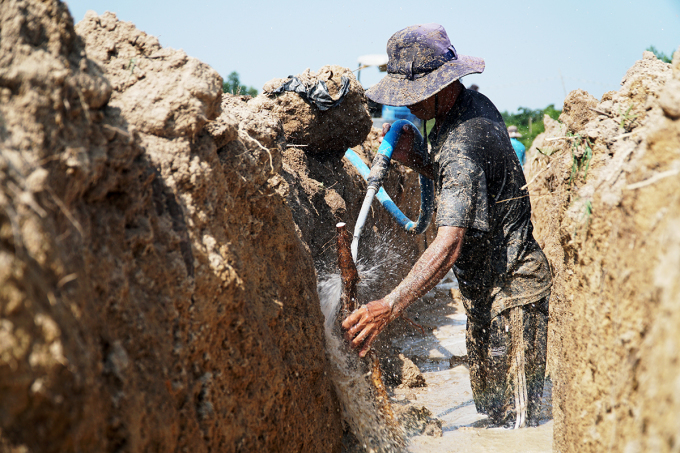 Người đàn ông đứng dưới rãnh xịt nước để tách khoai mài khỏi thành đất cát. Ảnh: Trường Hà